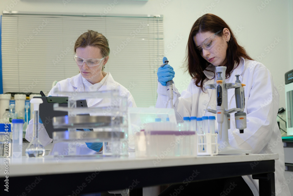 Fototapeta premium Two Female Scientists Working in Modern Research Laboratory with Pipette and Lab Equipment