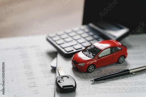 Fotografie Red car model with calculator, vehicle key, pen, and financial documents on office desk representing car financing, auto loan calculation, insurance payment, and automobile ownership process