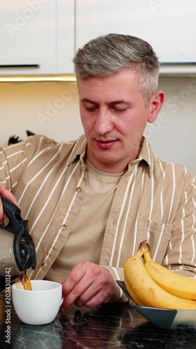 Middle-aged man pours coffee in kitchen at home with calm smile enjoying warm aroma and quiet breakfast break. Young adult guy starts morning with tasty drink feeling relaxed cozy and content indoors