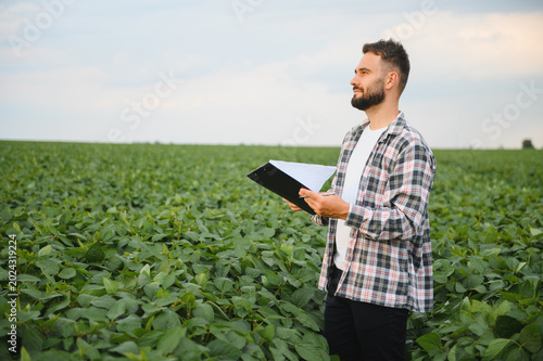Bild auf Leinwand Agronomist holding clipboard inspecting crops in soybean field