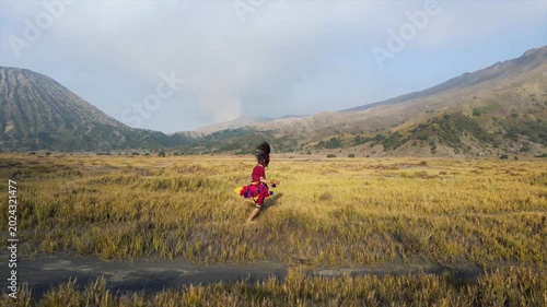 Traditional Indonesian dancer running across a wide savanna field with mountains in 4K resolution.
