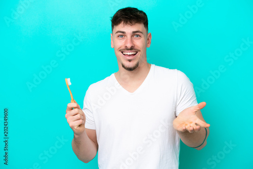 Foto Young caucasian man brushing teeth isolated on blue background with shocked faci