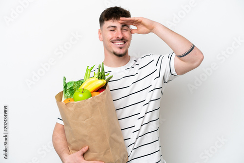 Obraz na plátně Young caucasian man holding a grocery shopping bag isolated on white background