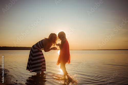 Mothers day. Mom and daughter have rest talking and walking together in water on sandy beach at sunset. Good relations between generations. Happy family pastime. Outdoor activities. Summer vacation.