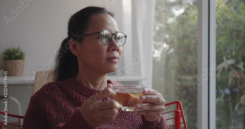 Asian Woman with glasses holding teacup by Window in Morning