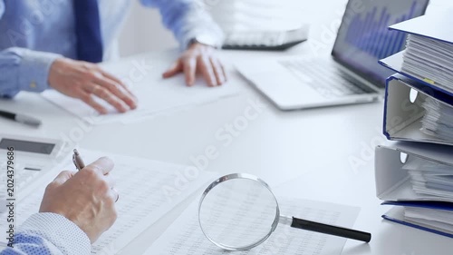 Accountants are analyzing financial reports with magnifying glass and documents, performing accounting and auditing tasks in the office, close up. Audit and taxes in business
