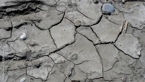Cracked Earth and Dry Mud Texture – Close-up. Detailed close-up shot of dried, cracked mud and clay soil with a few scattered pebbles. A powerful symbol of drought, aridity, and climate change. 