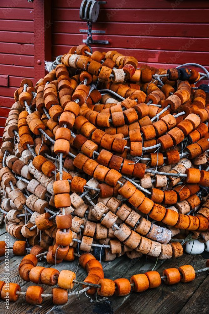 Obraz premium Close Up of Weathered Orange Fishing Net Floats Piled Against a Red Wooden Wall in Alaska