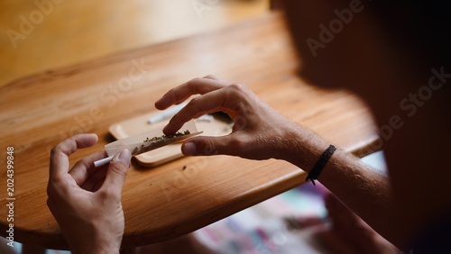 Bild auf Leinwand Person's hands rolling a cannabis joint on a wooden table