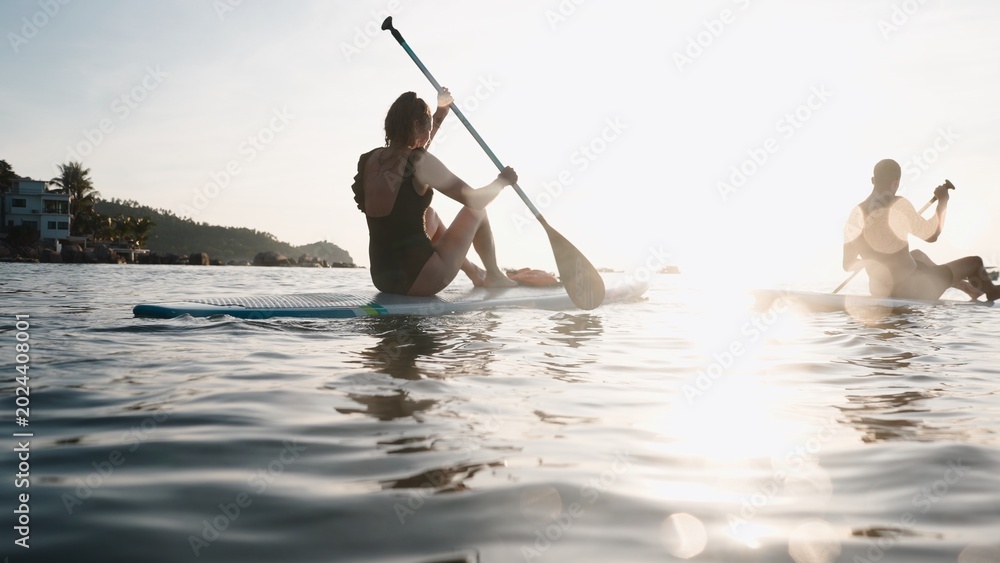 Fototapeta premium Couple paddleboarding enjoying tranquil ocean during tropical sunset vacation