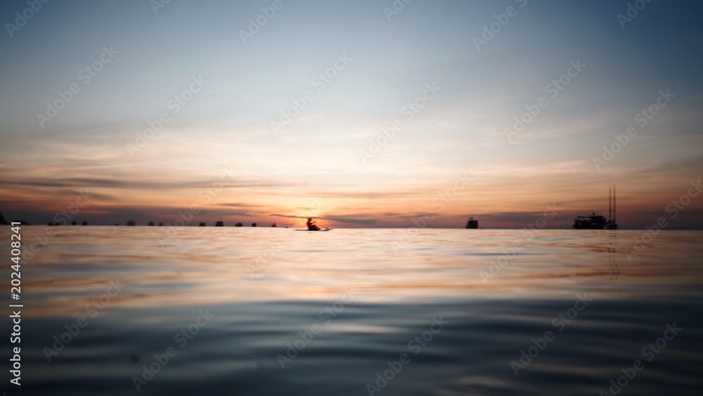 Fototapeta premium Paddleboarder relaxing on the water during a vibrant colorful sunset at sea