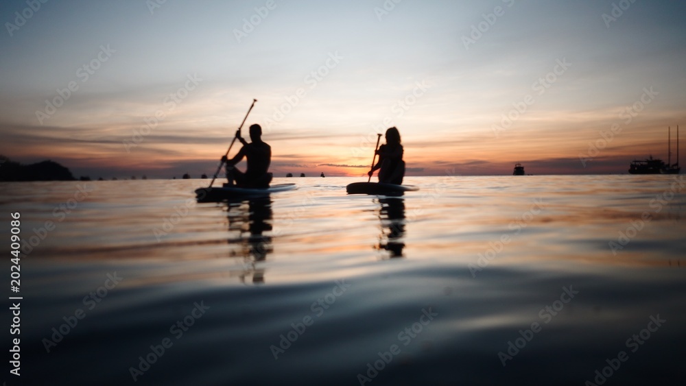 Fototapeta premium Couple paddleboarding during tropical sunset, enjoying romantic water adventure