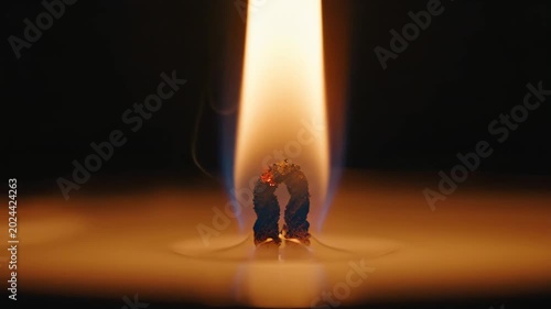 Extreme close-up of burning candle wick and flame against dark background. Glowing fire in molten wax creating warm light