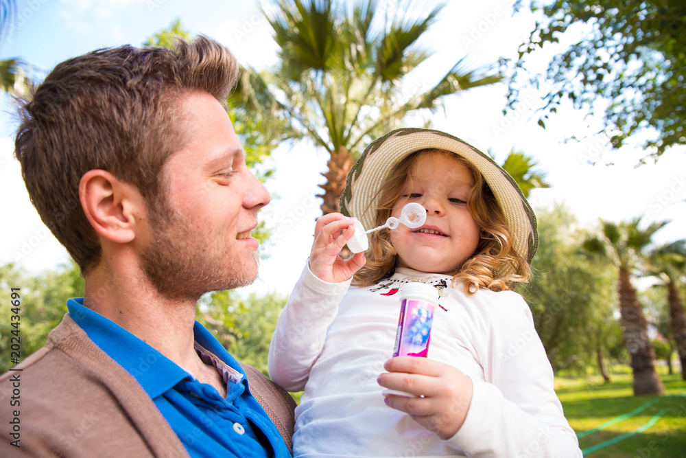 Fototapeta premium Father and daughter blowing bubbles in a tropical park