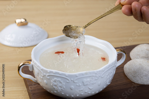 Fotografía A close-up shot of edible bird's nest soup with goji berries in an ornate white bowl, being scooped with a gold spoon