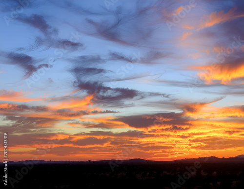A vibrant sunset paints the sky with fiery orange and blue hues, contrasting with the dark silhouette of distant mountains.