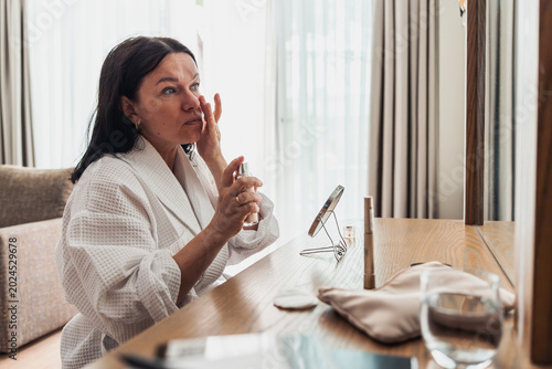 Tableau sur toile A middle-aged Caucasian woman with long dark hair applies skincare at a vanity