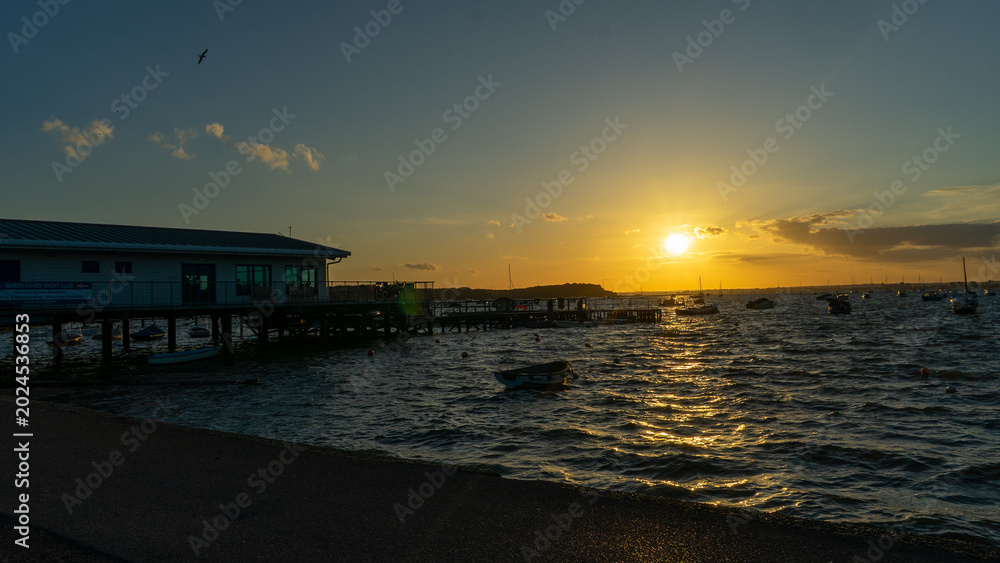 Fototapeta premium Calm waters and serene sunset over leisure boats at Sandbanks, Poole, Dorset near Bournemouth with foil surfers sailing through the wind.