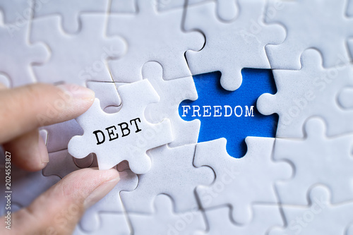 Konstfotografi Hand fitting Debt and Freedom blue puzzle pieces together on gray jigsaw backgro