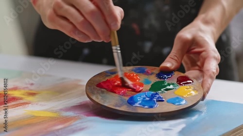 Tracking shot of artist hands mixing paint on wooden palette over canvas in studio close up