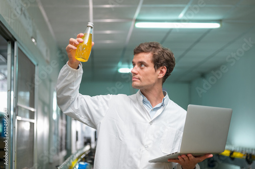 Scientist analyzing beverage sample in laboratory using laptop for quality control and research.