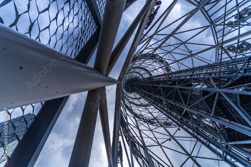 Looking up inside steel lattice communication tower under cloudy sky
