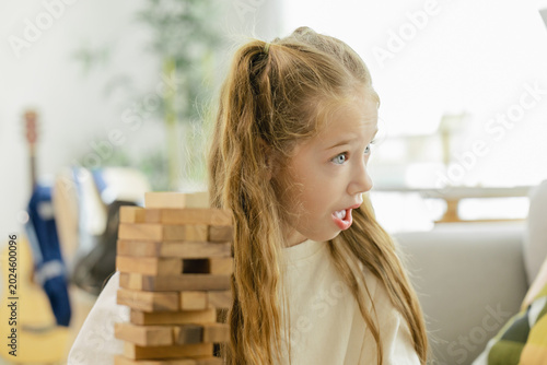 Foto A young girl looks shocked while playing a game of wooden block stacking, reacting to a critical moment in the game