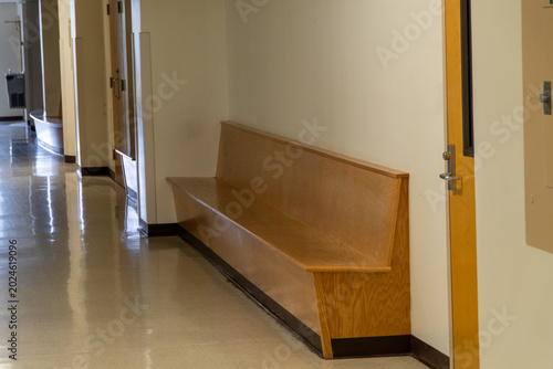 Photos Long empty wooden bench in a quiet school or office hallway with shiny tiled floors and a drinking fountain in the background, suggesting waiting, contemplation, or a break area