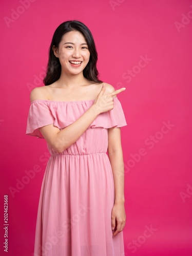 Happy young woman pointing finger at pink background