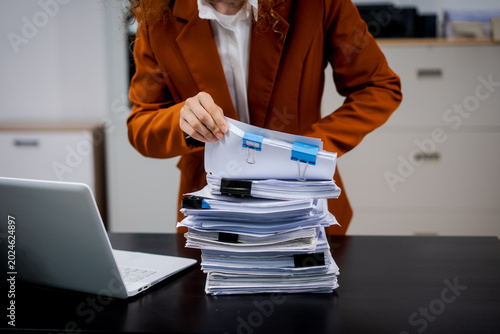 Businesswoman handling a thick stack of paperwork on a desk beside a laptop in an office, symbolizing bureaucracy, workload, and document management.