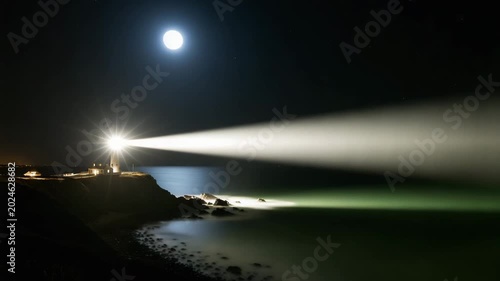 Nighttime lighthouse emitting light beam over rocky coastline  