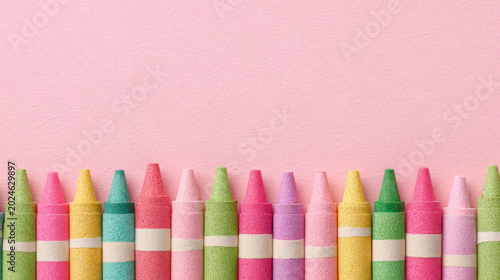 A row of colorful crayons lined up at the bottom against a solid light pink background, leaving ample copy space above for text or designs.
