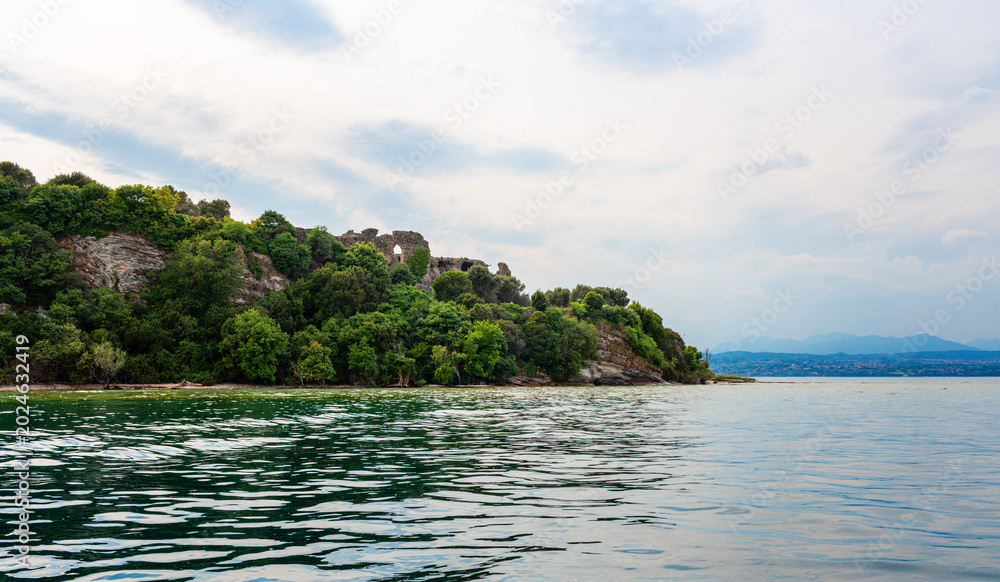 Obraz premium Scenic view of Lago Garda Ruins in Sirmione Italy calm waters, and a cloudy sky, showcasing the natural beauty of the region's landscape