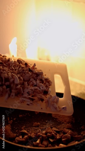 Faceless woman adding chopped mushrooms to sautéed onions in frying pan in cozy candlelit kitchen