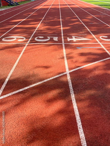 Vertical perspective of red rubber running track lane number with start lines. Authentic outdoor stadium, ideal for sports competition, racing background, and athletic training concepts.