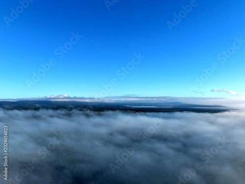 Fotografía defaultFotografia aérea capturada por drone mostrando um mar de nuvens brancas sob um céu azul limpo com o sol brilhando intensamente ao centro