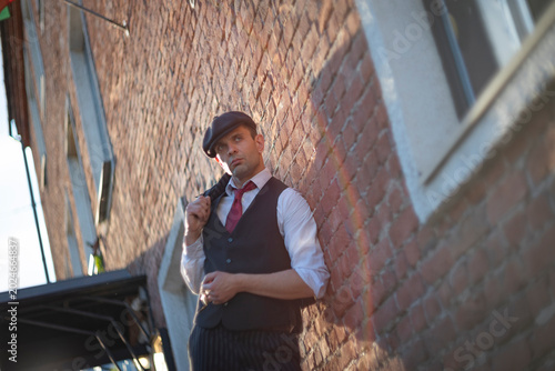 Obraz na płótnie Thoughtful retro man in newsboy cap leaning against brick wall with copy space