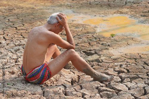 Foto Drought's Despair: A man sits dejected in a parched, cracked earth landscape, a symbol of the devastating impact of drought and environmental hardship