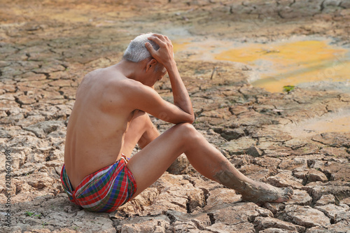 Fotografia Despair in Drought: A parched man sits defeated on cracked, arid earth, a poignant symbol of environmental devastation and human struggle against drought