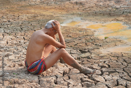 Canvas Print Drought Despair: An elderly man, visibly distressed, sits amidst parched, cracked earth and a small, stagnant pool, symbolizing the devastating effects of extreme drought