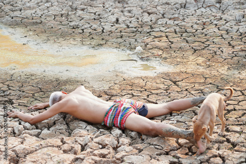 Fotografia Victim of Drought: A lone figure lies prostrate on cracked, dry earth, accompanied by a dog, a stark depiction of the devastating impact of drought and water scarcity