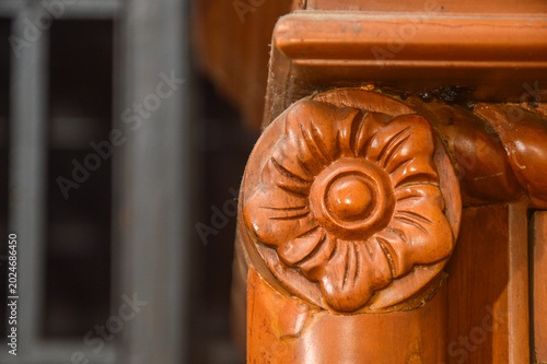 Close up of hand carved floral ornament on traditional brown wooden furniture. Detailed flower carving relief on teak timber pillar decoration.