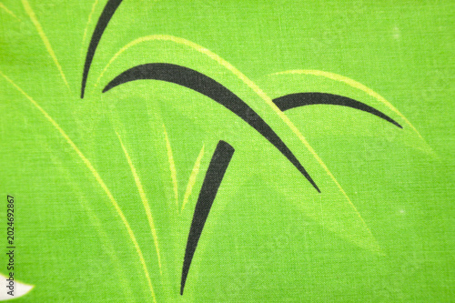 Full frame of bright green fabric with printed leaf pattern. Seamless tropical textile texture with black and light green plant ornaments on cloth surface.