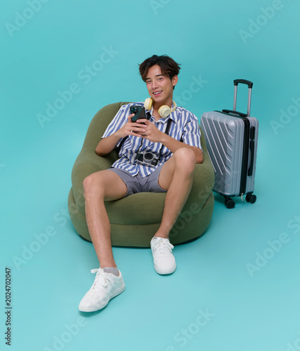 Young asian traveler using smartphone while relaxing with luggage and camera modern travel lifestyle vacation planning digital connectivity and leisure tourism experience.