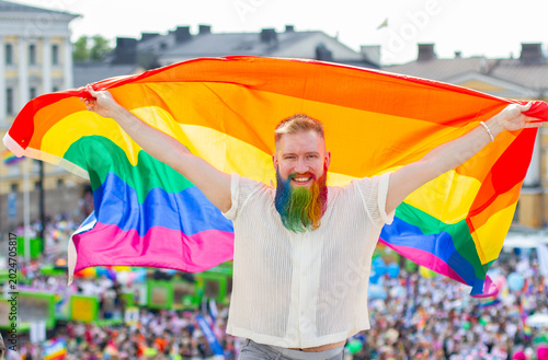 Happy homosexual bearded man with rainbow flag on Pride background