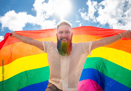 young happy homosexual man with rainbow flag on sky background