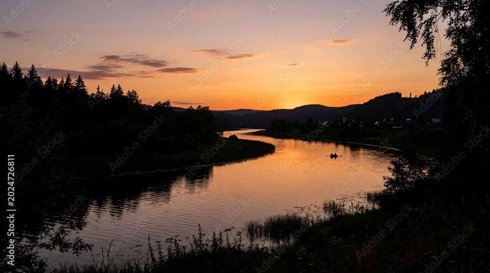 Obraz premium A serene winding river flowing through a dark forest at sunset.