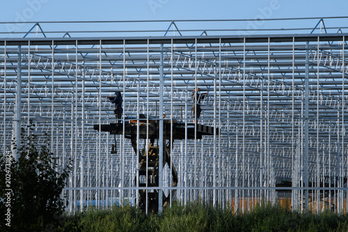 Men on a lift working on the metal construction of a glass greenhouse for tomato cultivation