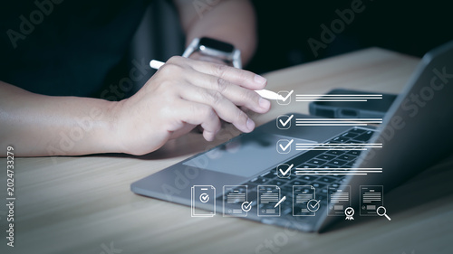 Businessperson hand using stylus pen to check virtual digital document checklist on laptop computer for smart paperless office management and corporate compliance process.