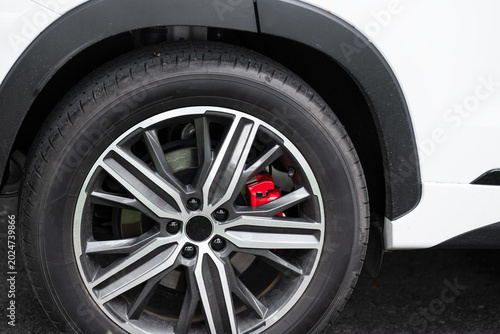 Modern crossover car wheel with stylish dual-tone alloy rim and bright red brake calipers close-up.  Close-up of a modern white SUV car wheel  